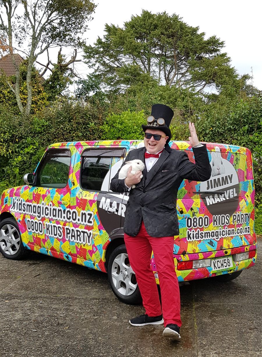 Jimmy Marvel holding a white rabbit in front of his brightly wrapped magic car