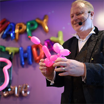 Jimmy Marvel twisting a bright pink poodle balloon